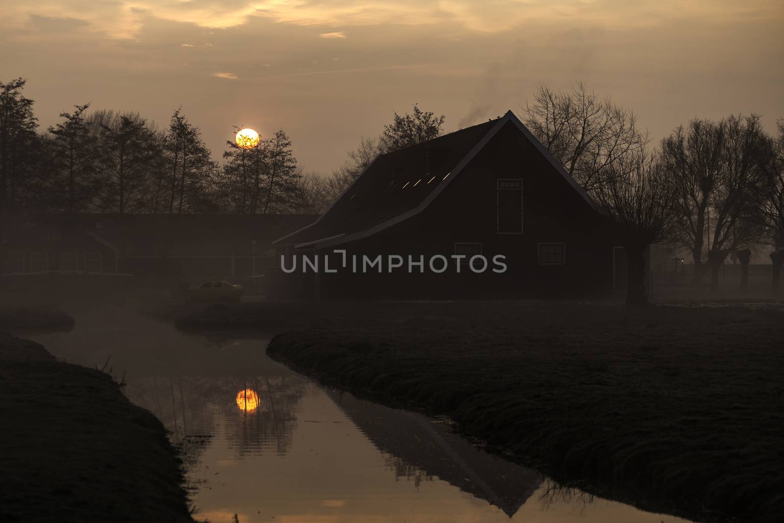 Beautiful typical Dutch wooden houses architecture at the sunrise moment mirrored on the calm canal of Zaanse Schans located in the North of Amsterdam, Netherlands