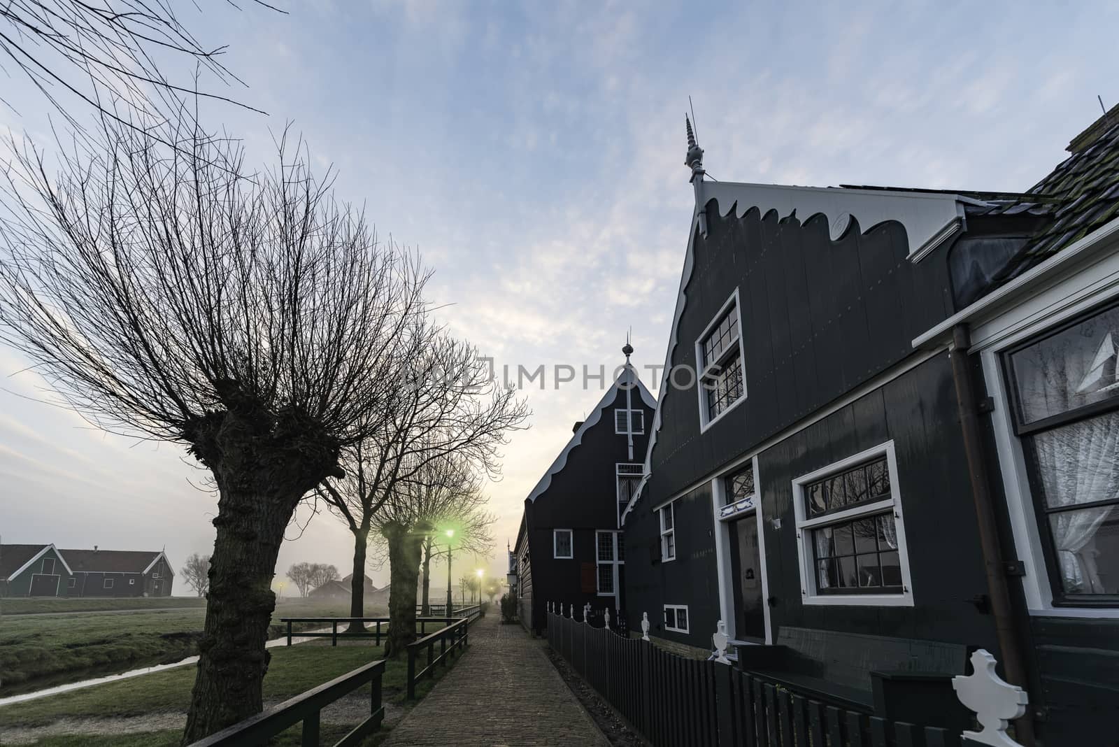Hanging lamppost Beautiful typical Dutch wooden houses architecture at the sunrise moment mirrored on the calm canal of Zaanse Schans located in the North of Amsterdam, Netherlands by ankorlight