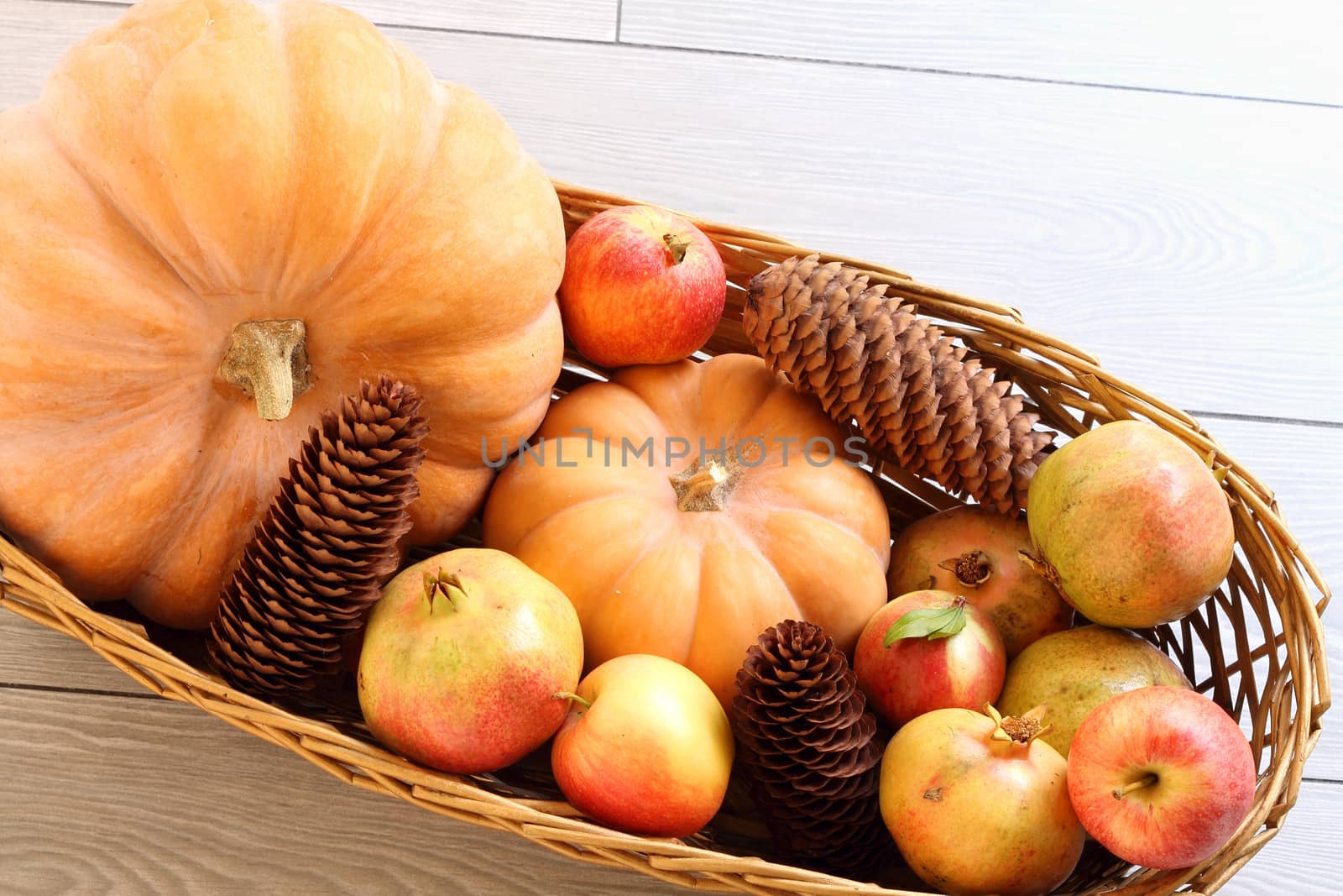 Basket with autumn pumpkins, pomegranates, pinecones and apples