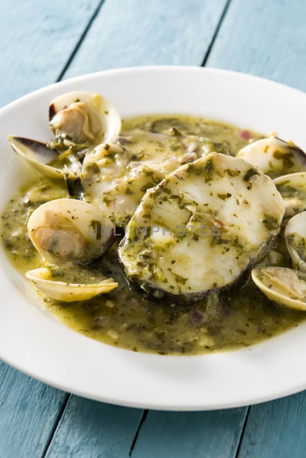 Hake fish and clams with green sauce on blue wooden background