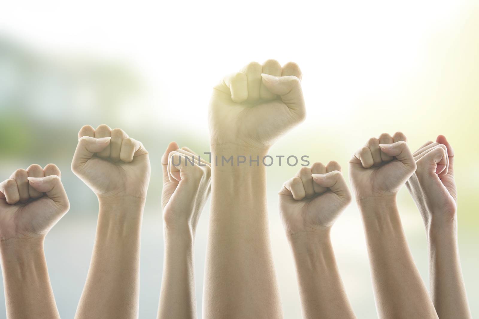 People in city raised fists in the air, sunlight background. victory and protest