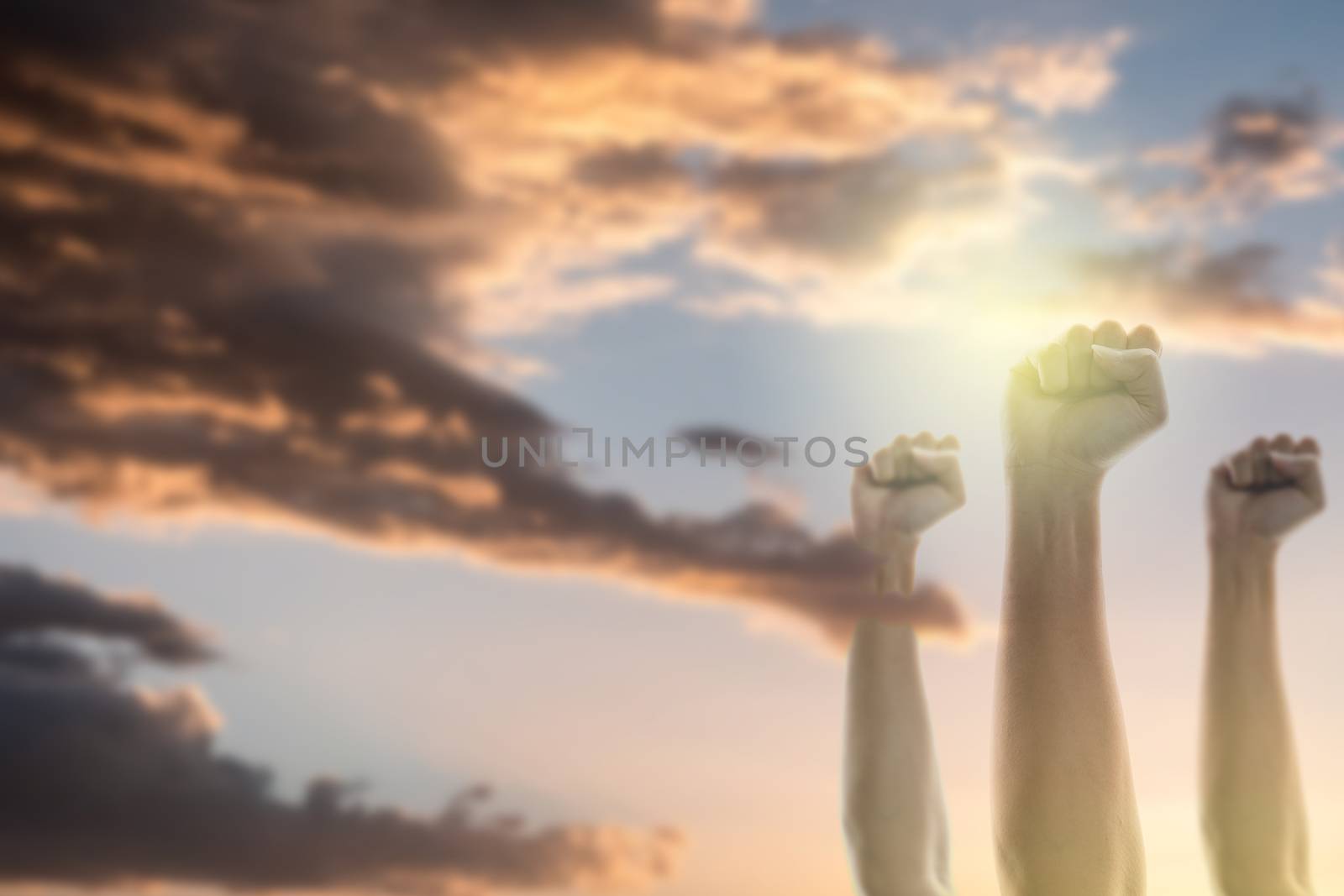 Fists of people raised in the air with sky and sunlight background.