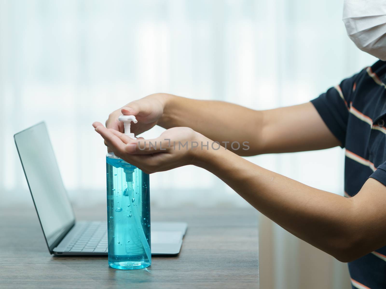 Man worker wear protective face mask cleaning her hands with sanitizer liquid antibacterial gel, working from home in quarantine, corona virus concept.
