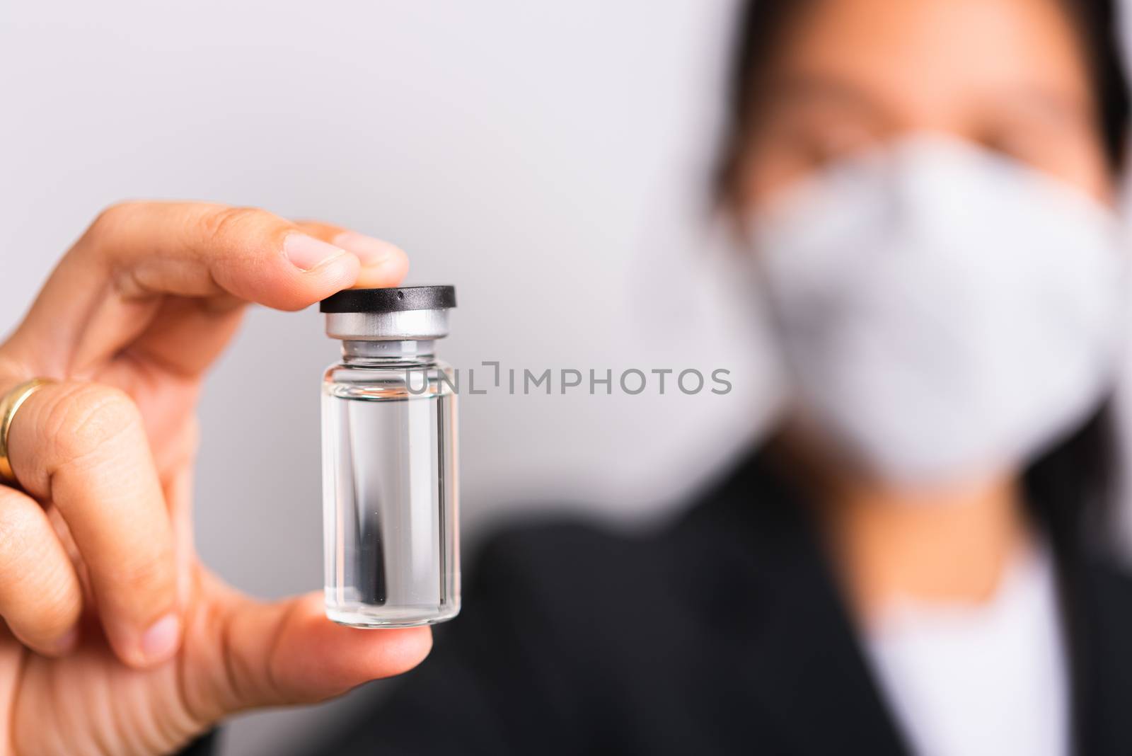 Asian woman doctor wearing surgical protective cloth face mask against coronavirus her hold ampoule bottle vaccine focus on  glass transparent, studio shot isolated white background, COVID-19 concept