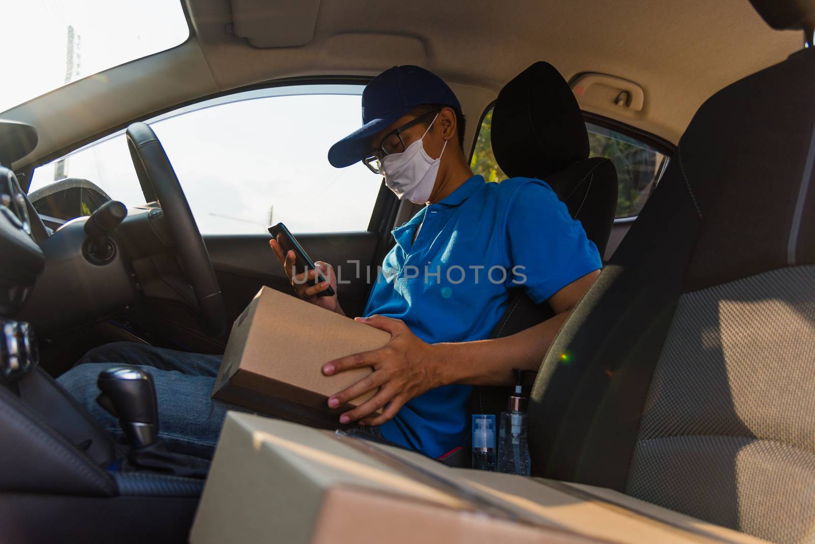 Asian delivery man courier online holding deliveries out boxes in car and using mobile phone contact the customer he protective face mask service under curfew quarantine pandemic coronavirus COVID-19