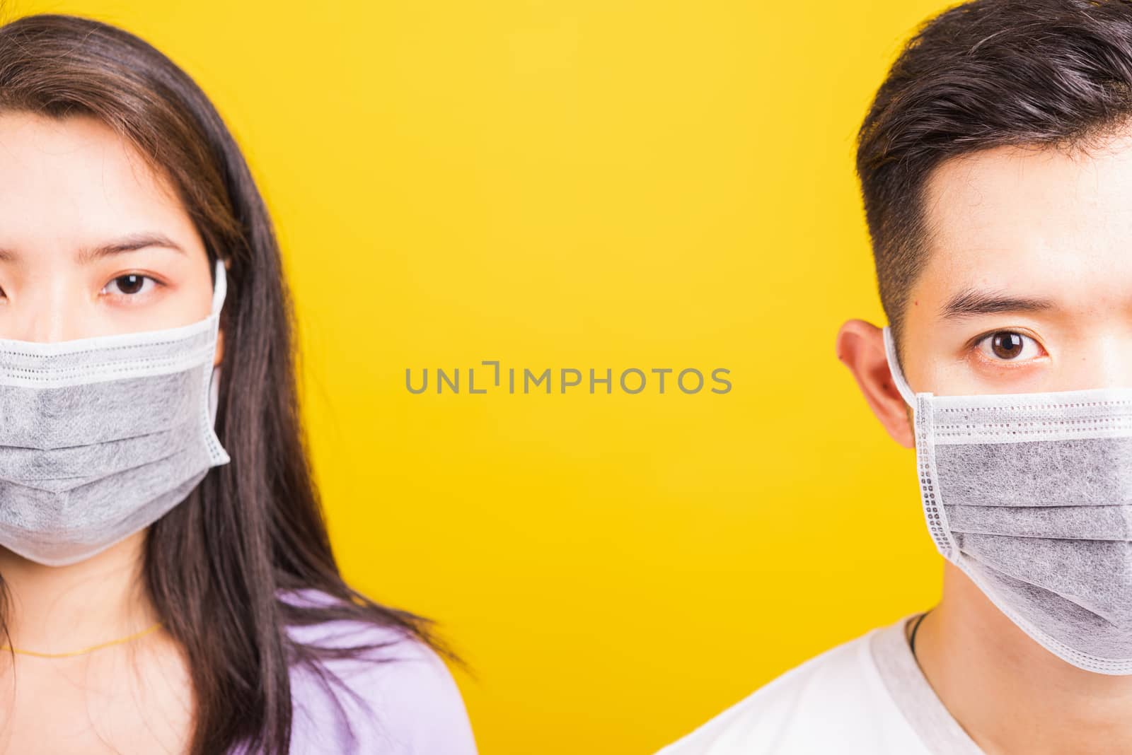 Asian beautiful woman and handsome man wearing protection face mask against coronavirus, looking to camera, studio shot isolated on yellow background with copy space, COVID-19 or corona virus concept