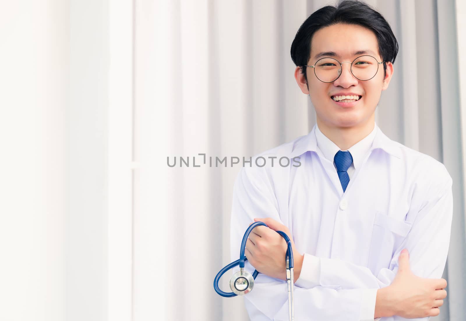 Portrait closeup of Happy Asian young doctor handsome man smiling in uniform stand crossed arm hold stethoscope on hand looking to camera with cop space, healthcare medicine concept