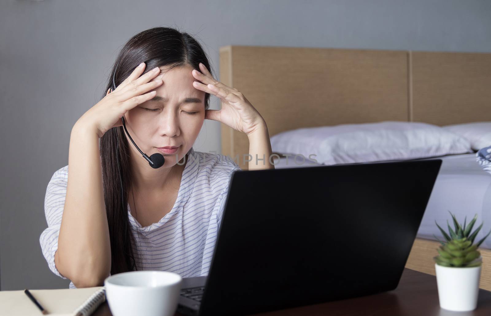 Asian woman working at home with headset making video conference with colleagues via laptop computer with stress emotion during transmission of COVID-19 Coronavirus outbreak, the new normal concept
