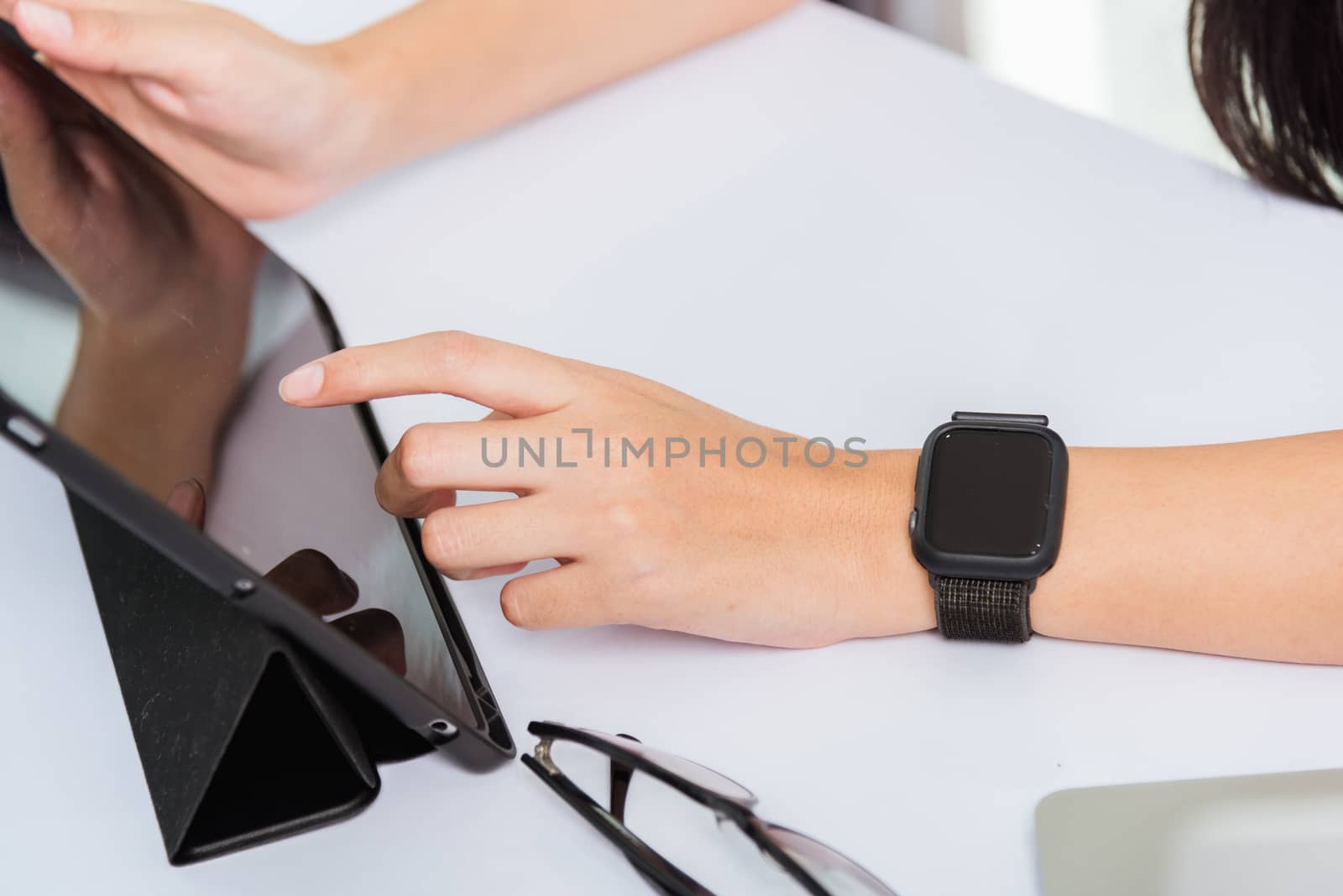 Work from home, Happy Asian young businesswoman use hand finger touch screen modern digital smart tablet computer she wears a smart watch on the wrist focus on smartwatch