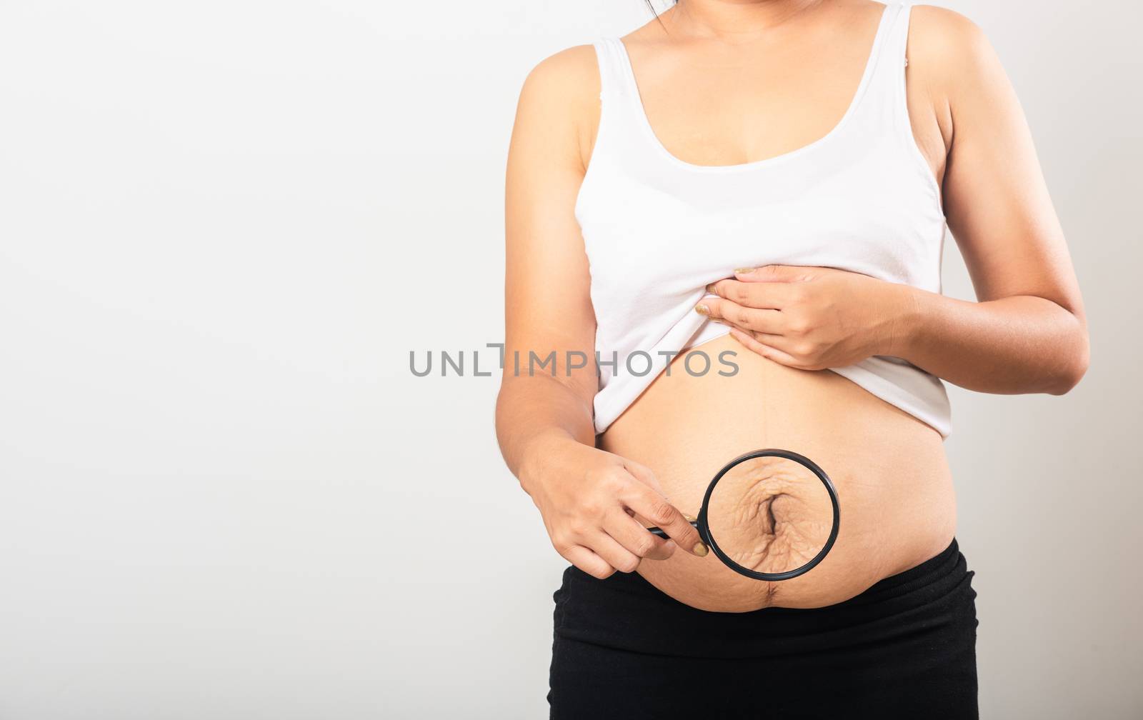Close up of Asian mother woman use magnifying glass show stretch mark loose lower abdomen skin she fat after pregnancy baby birth isolated on white background, Healthy belly excess body concept