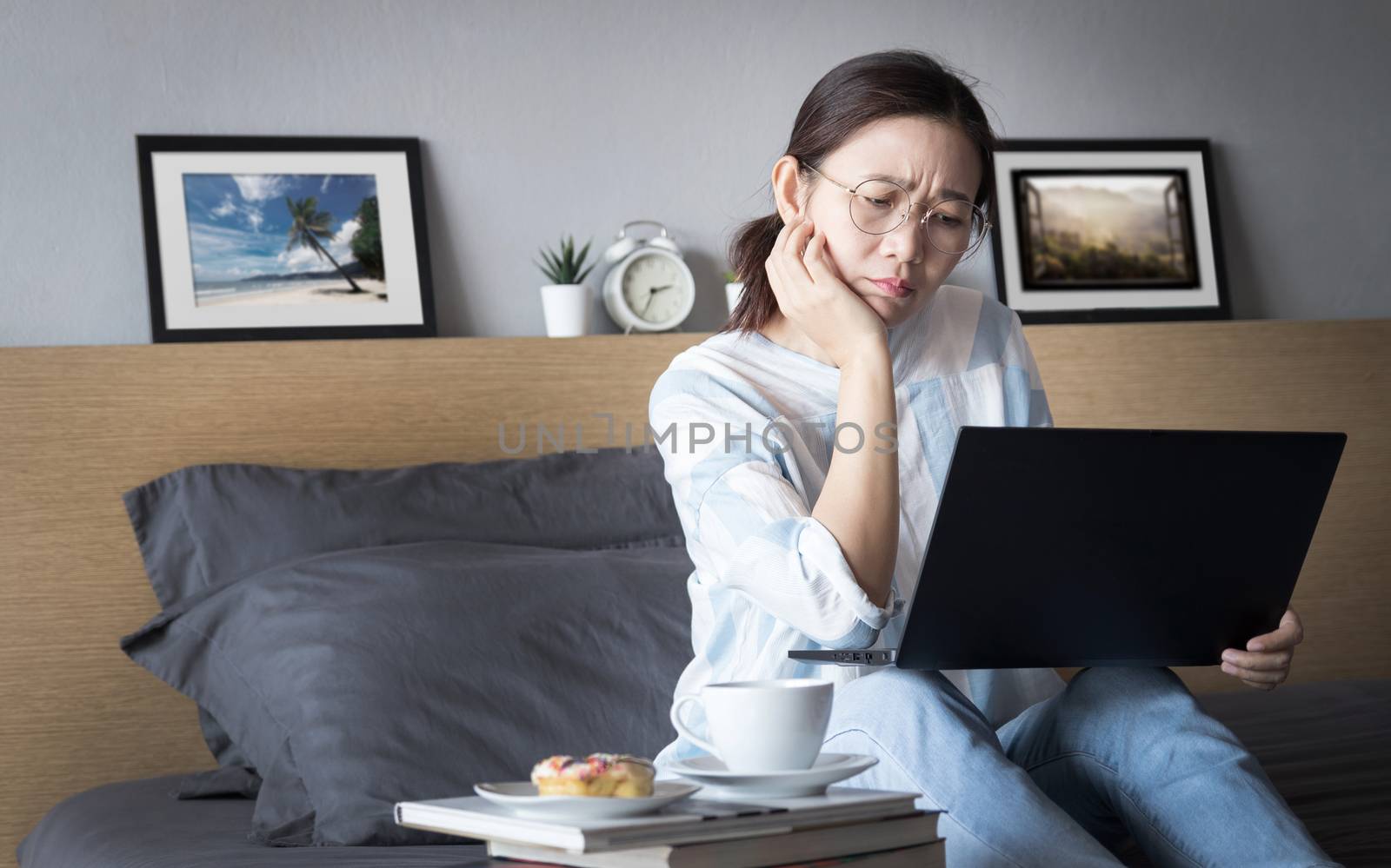 working from home, new normal concept. woman working with laptop computer on bed from her room during self isolation with stress emotion during transmission of COVID-19 Coronavirus pandemic by asiandelight