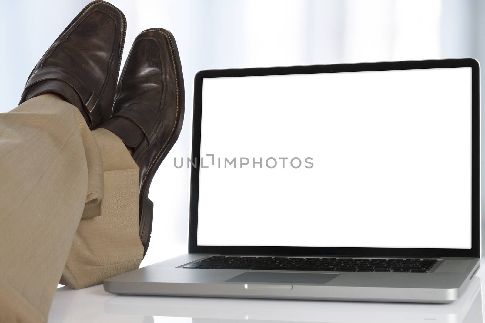 Businessman sits with his feet on the table next to a laptop with white screen.
