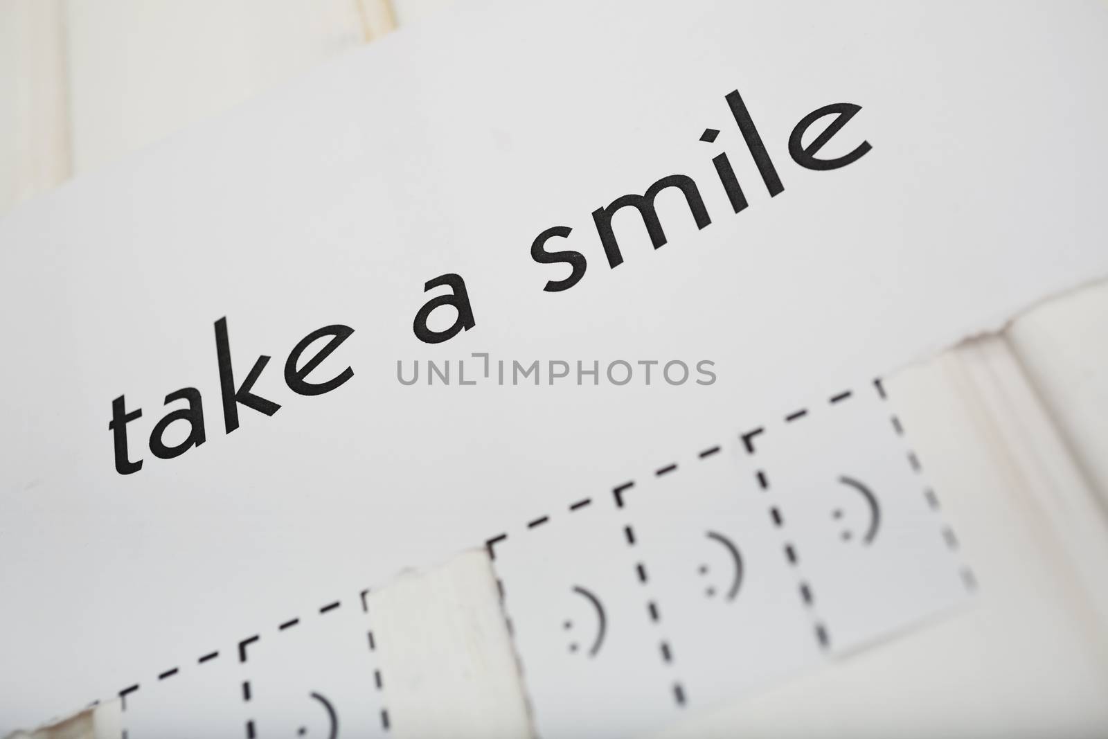 A paper with the phrase: Take a Smile and with a smile sign ready to be tore off. DOF. The focus is on the phrase.