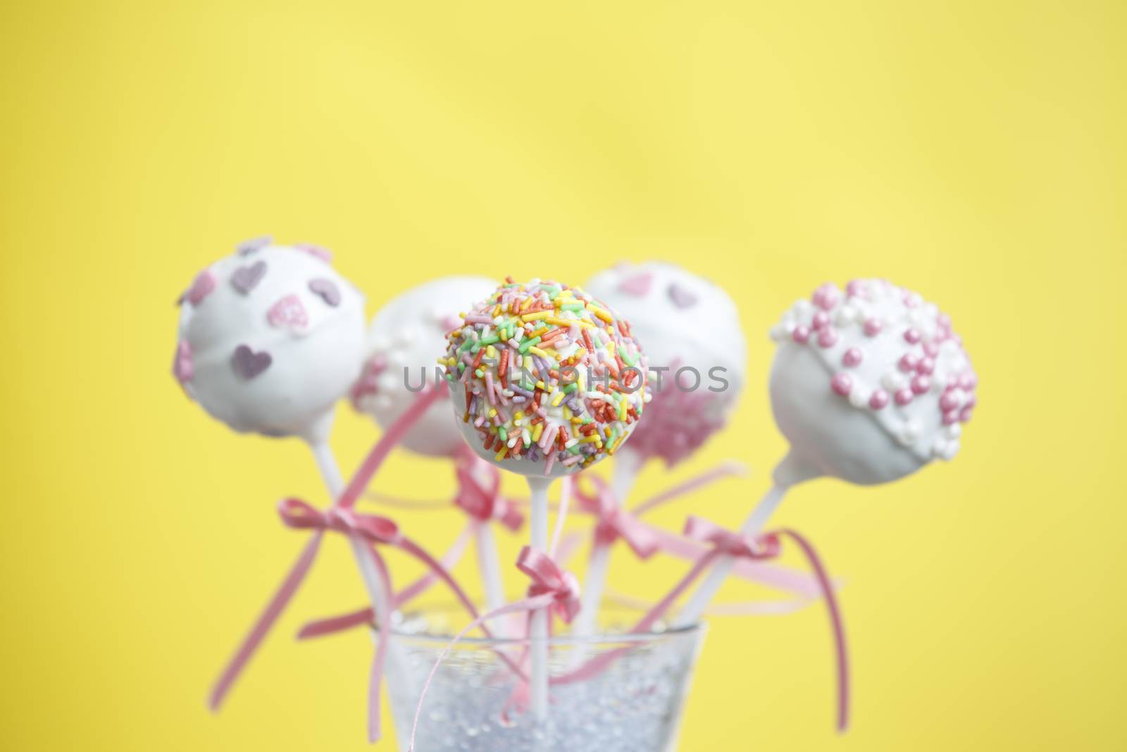 Cakepops over yellow background with pink ribbon.