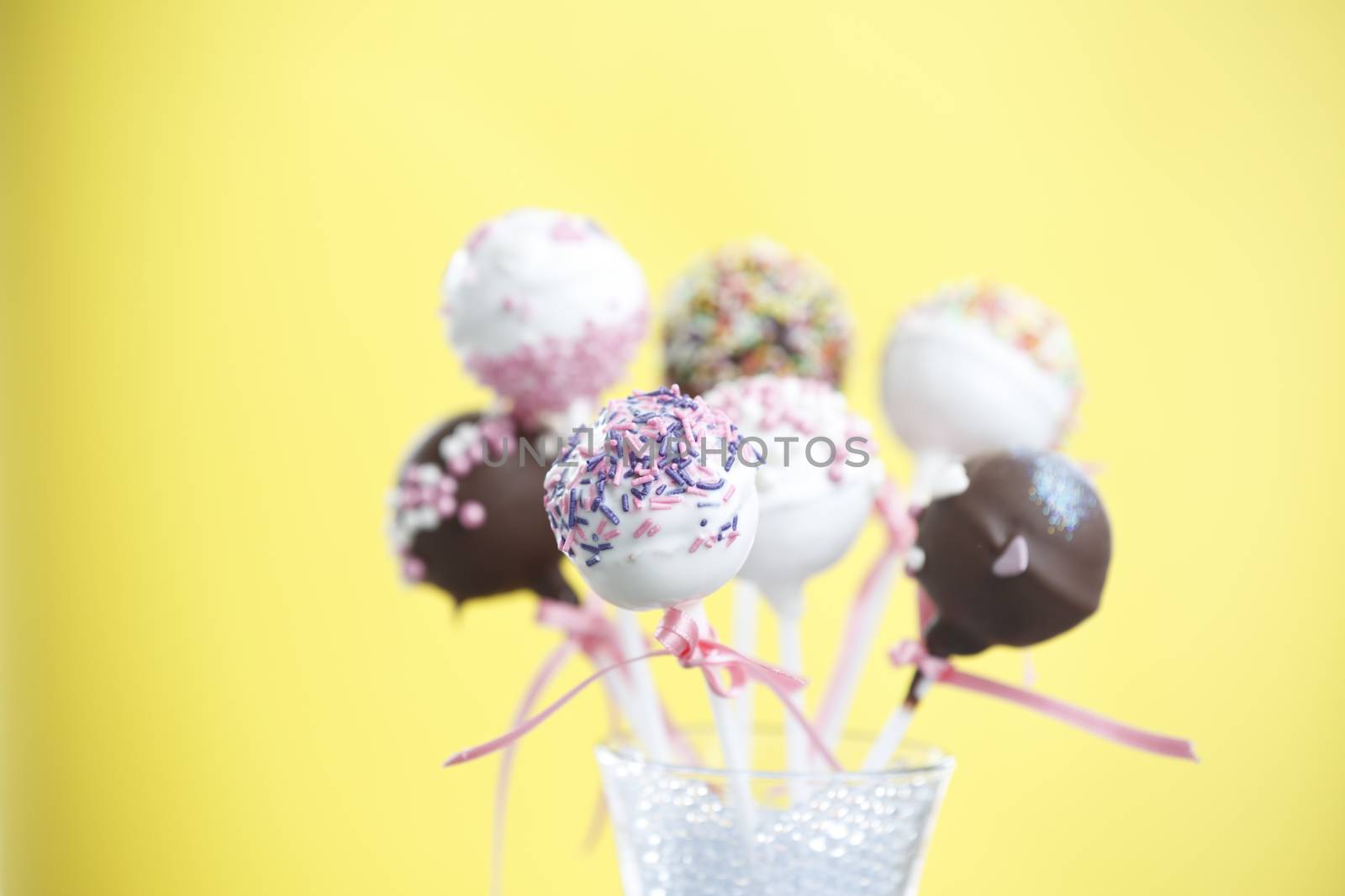 Cakepops over yellow background with pink ribbon.