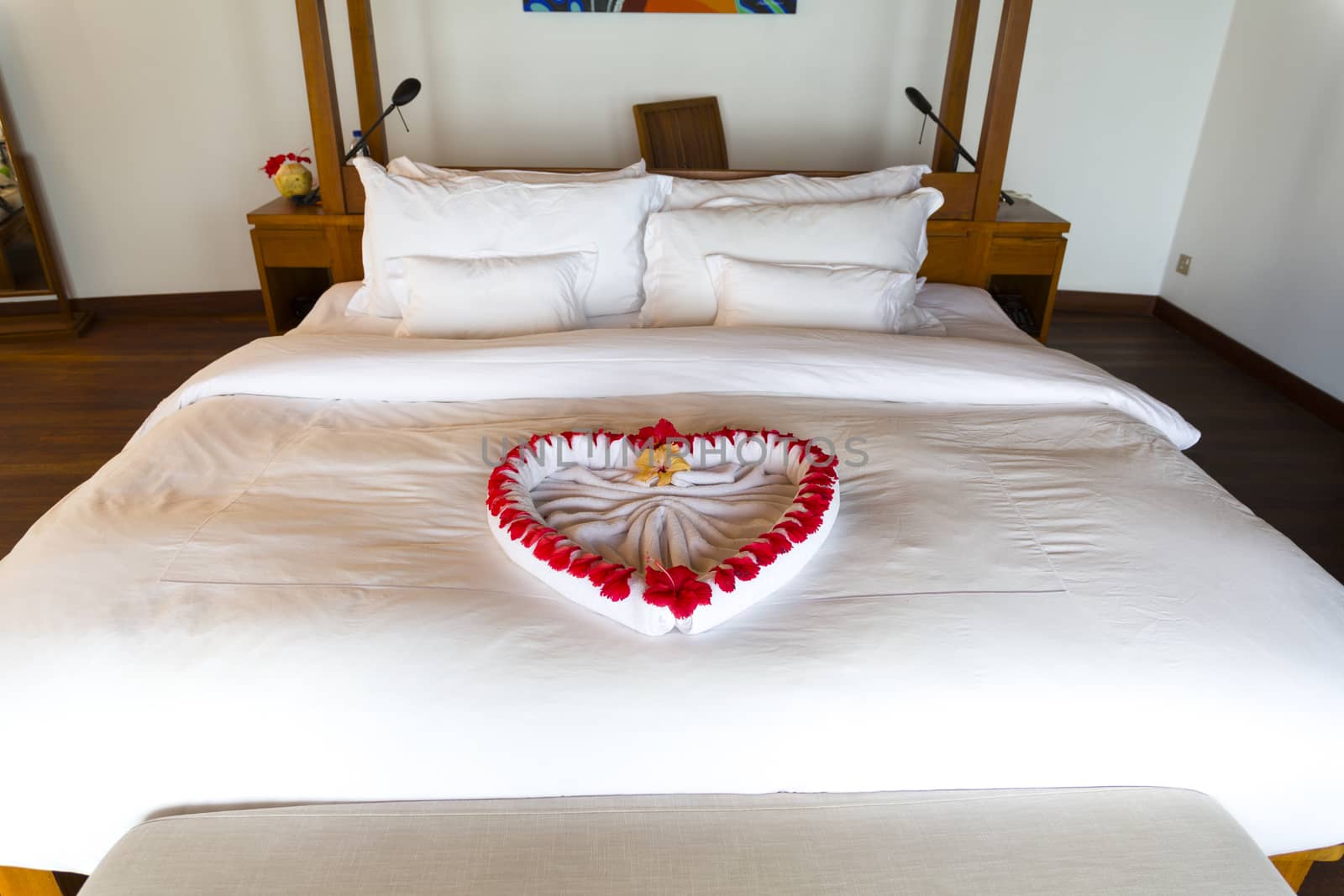 Towel forms a beautiful heart decorated with red flowers in a Luxury Resort room in Maldives. The heart is in the middle of the bed, the floor is wooden made.