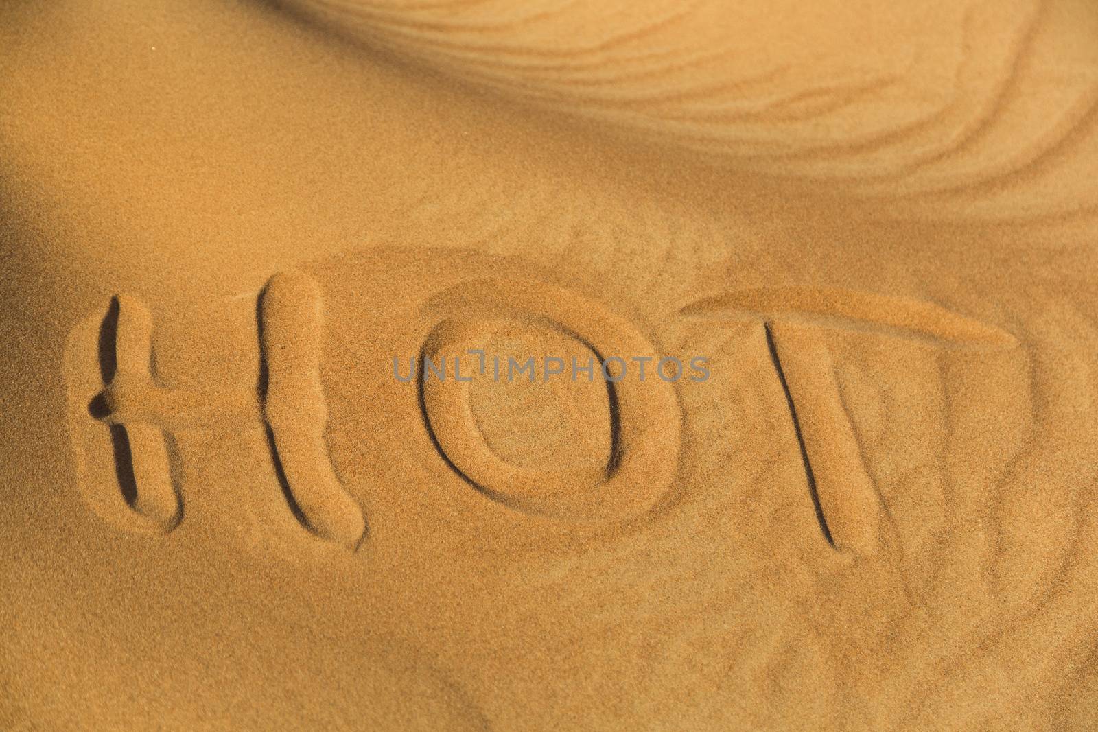 The word hot writen on the sand in desert.