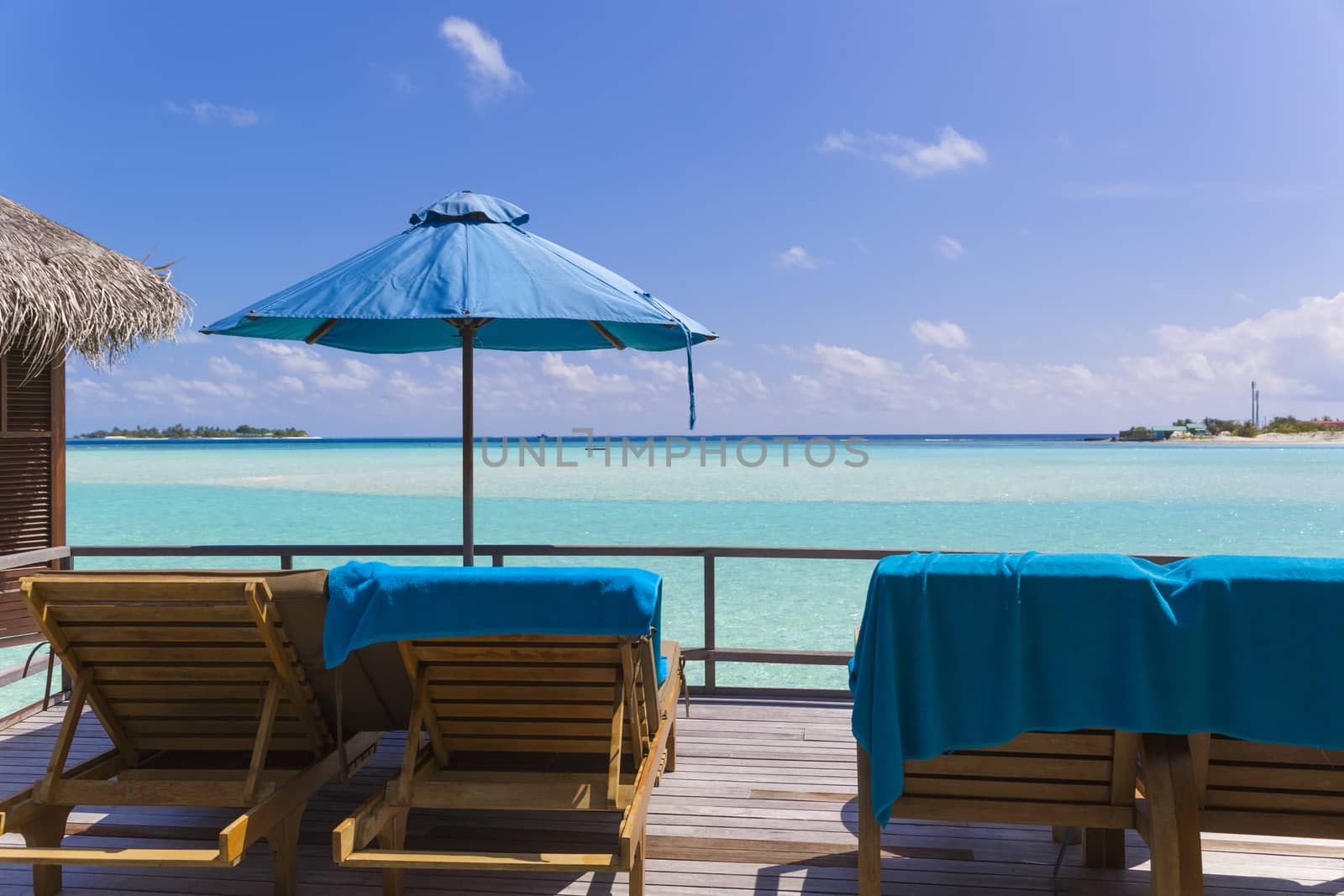 View from the deck of the bungalow  in The Maldives. On the deck there are deck chairs and beach umbrella. It is a beuatiful view of the sea, the water is clear, turquoise and in a strong contrast depending on the depth.