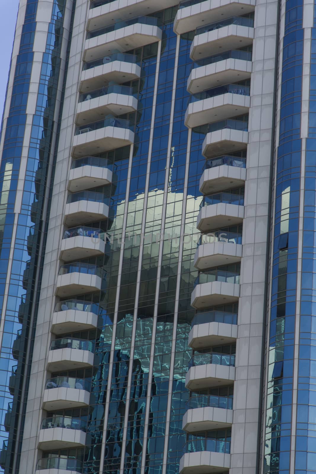 There is a building reflected on the surface of another building. The main building is mirrored and actual modern design. The blue color gives a business look.