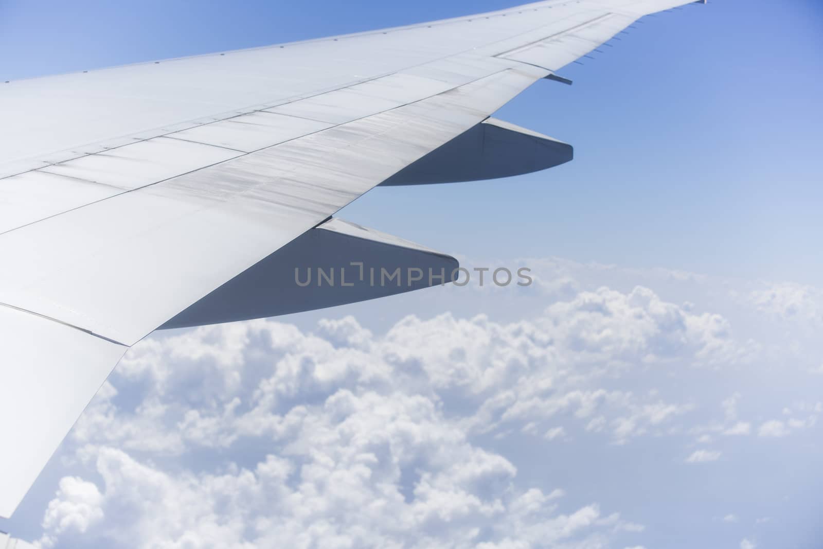 View from the right side of an aircraft of the wing, the plane is ready to land. It is a sunny day with a clear blue sky with clouds beneath it.