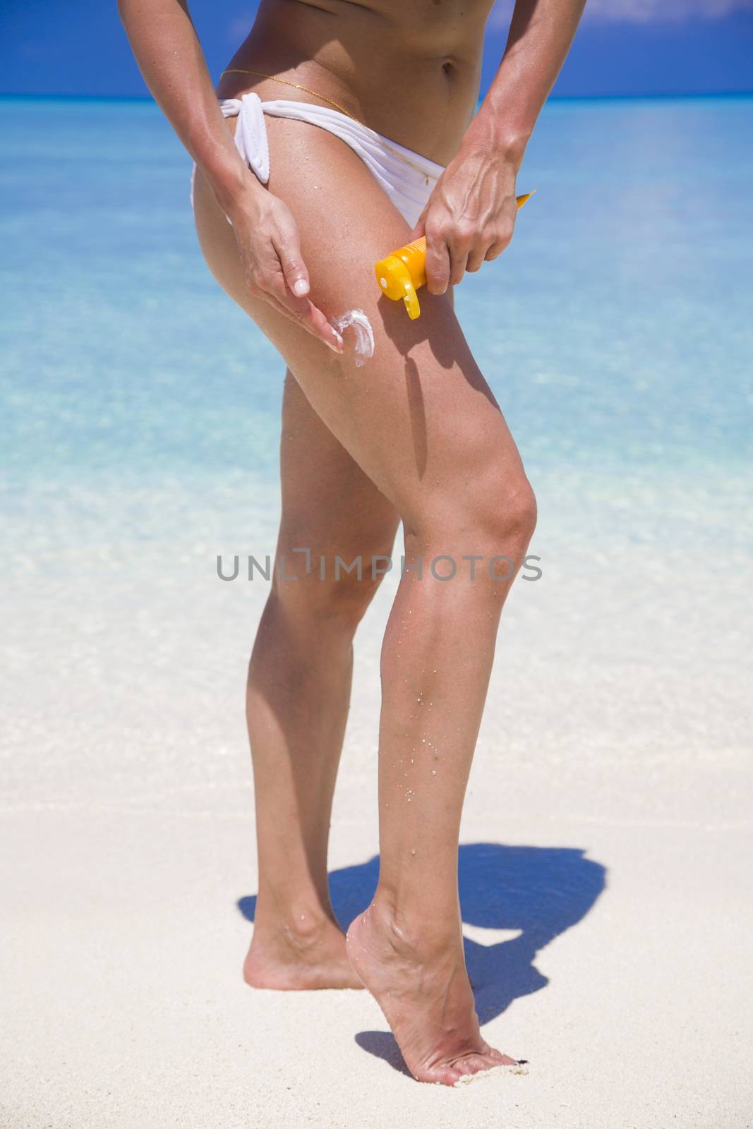 Woman applying sunscreen in front of the beach.