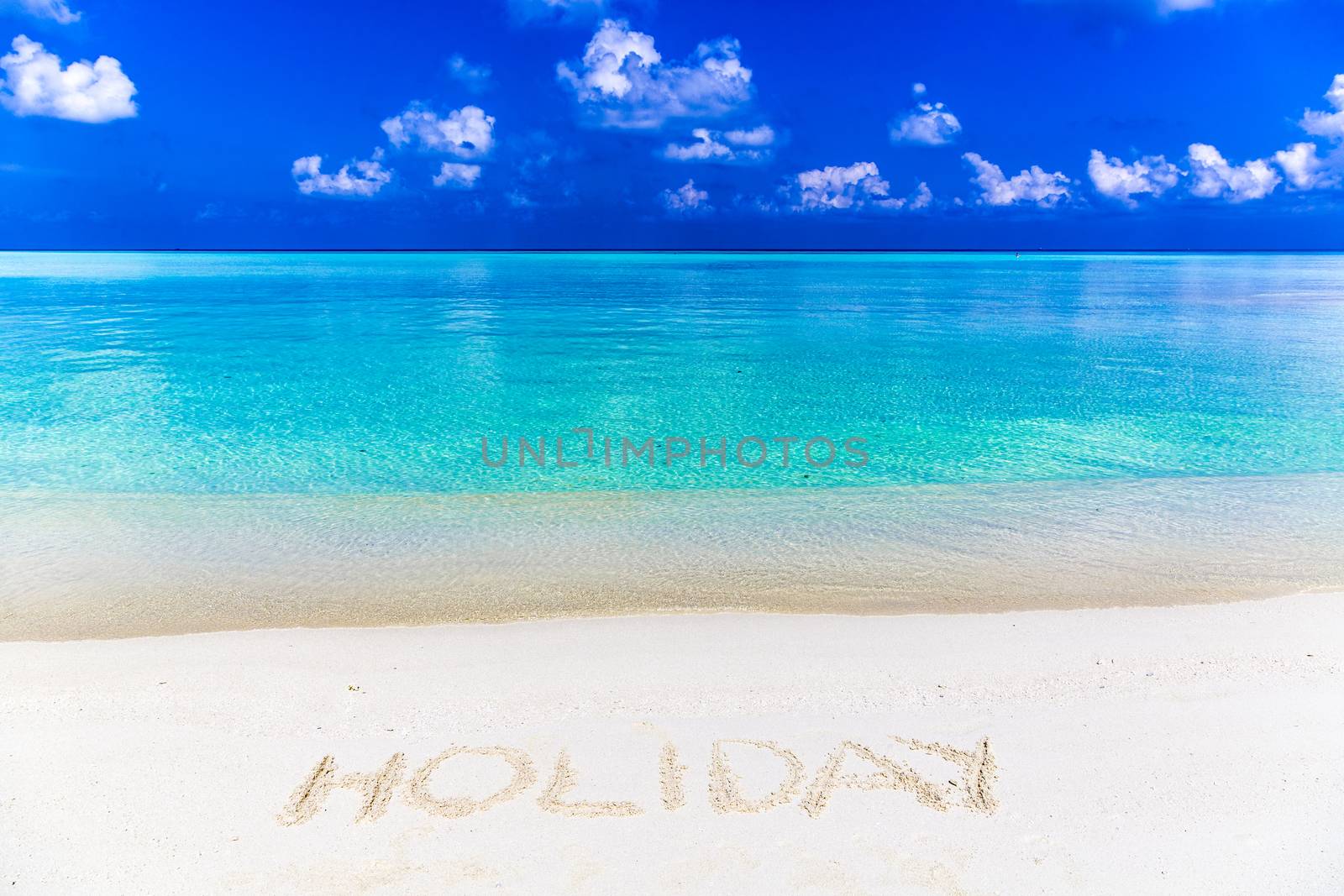 Word holiday written on sand in Maldives with the lagoon at background.
