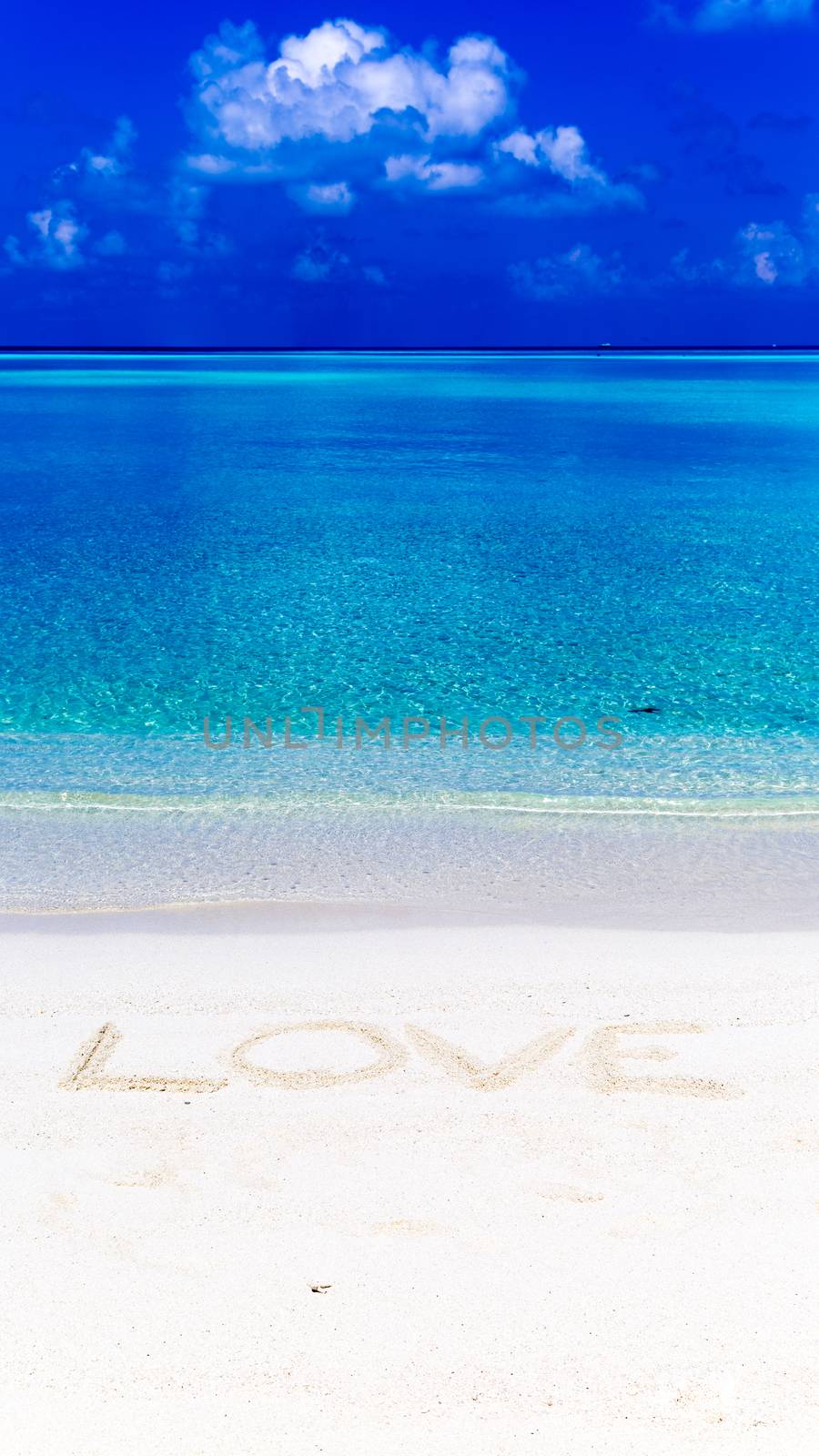 Word love written on sand in Maldives with the lagoon at background.