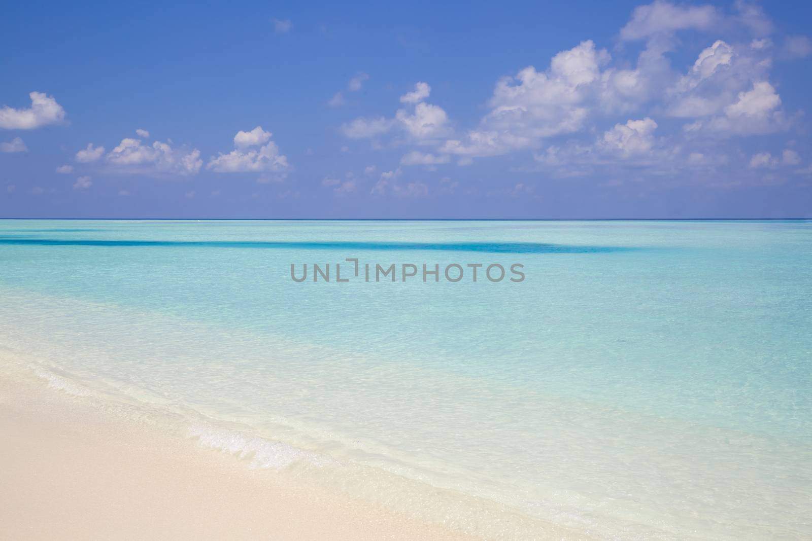 Tropical beach in paradise with clear crystal water in Maldives. Beautiful tones of turquoise in the sea. The sky is partial covered with clouds.