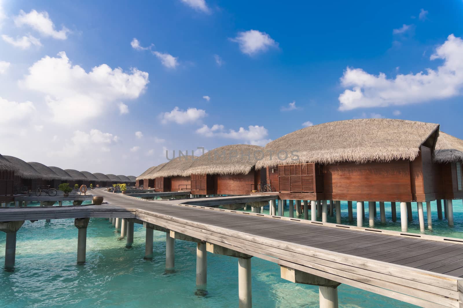 Luxury hotel with a line of bungalows over the water and a wooden path between them.