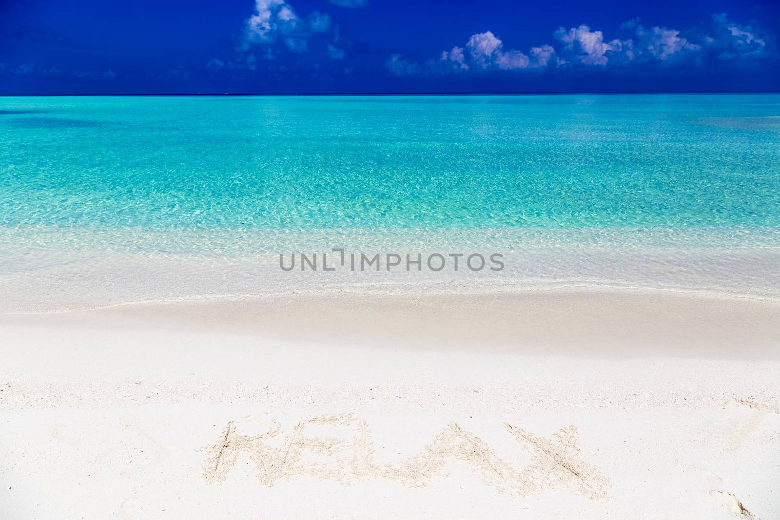 Word relax written on sand in Maldives with the lagoon at background.