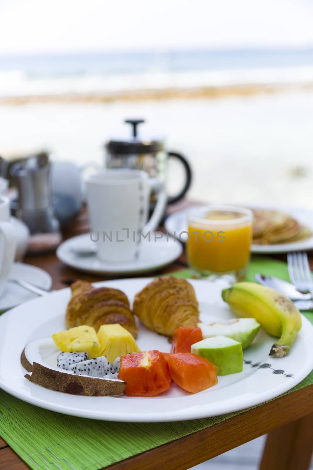 Delicious healthy breaklfast outdoors in a wooden table with sea at background. The breakfast consists of fresh fruit and waffles with pancakes.