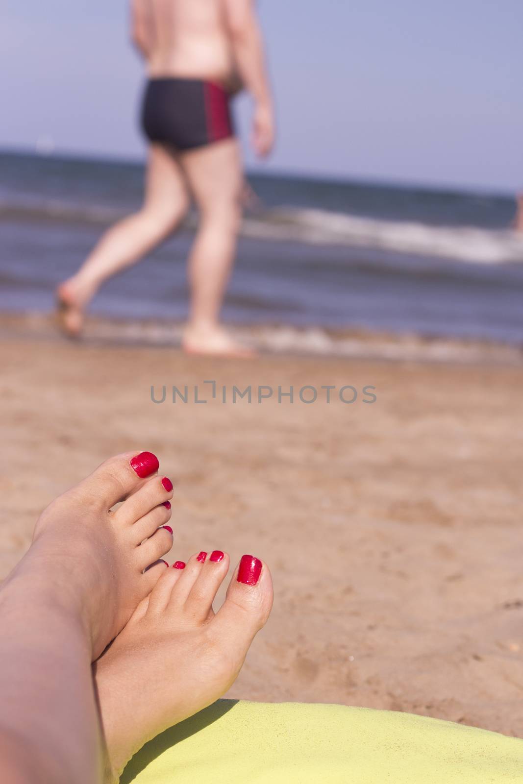 Beach scene with woman feet on the sand. Nails of feet painted red
