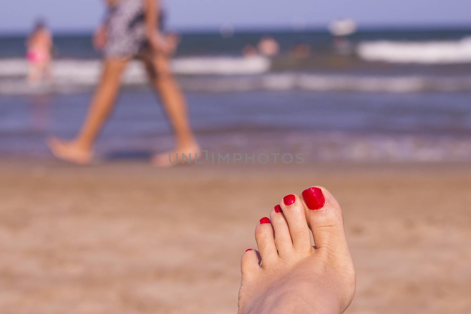 Beach scene with woman feet on the sand. Nails of feet painted red
