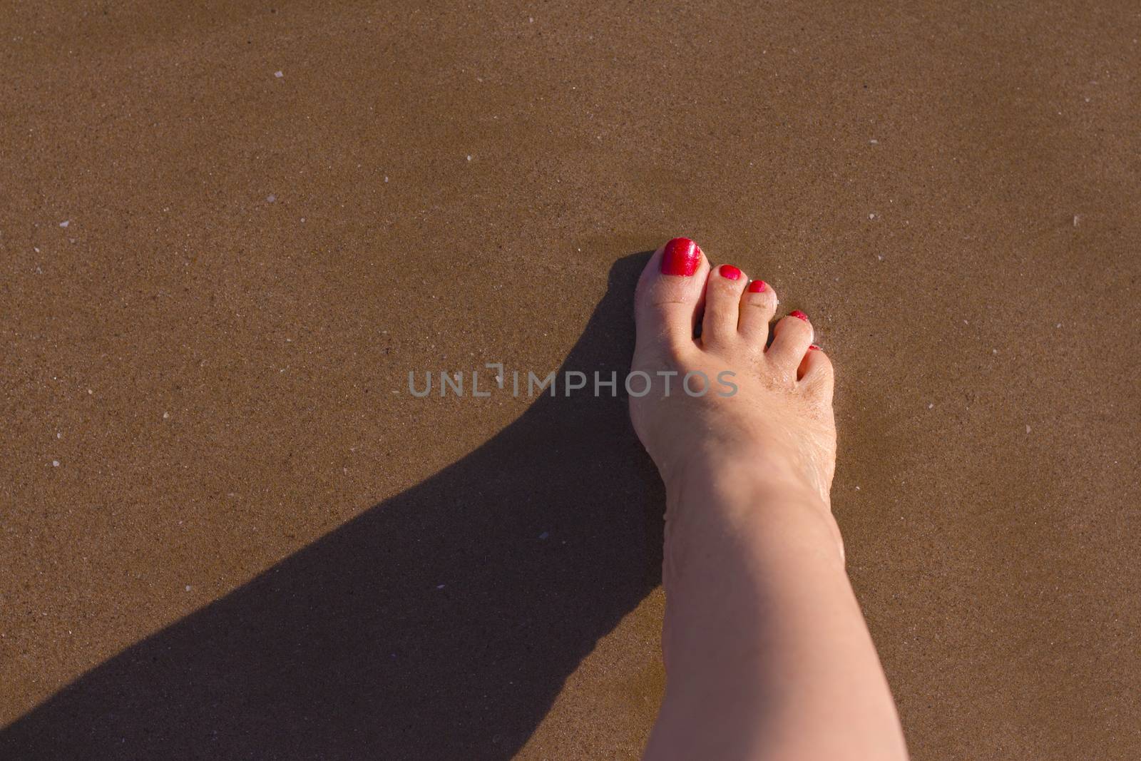 Beach scene with woman feet on the sand. Nails of feet painted red