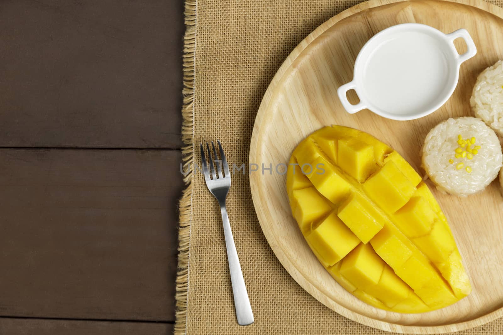 Top view Yellow half  mango with small fork. Mango fruit cubes on the wooden table. Tropical fruit asia. Fresh yellow mango peel and Sliced cubes on wood butcher. Dessert fruit.