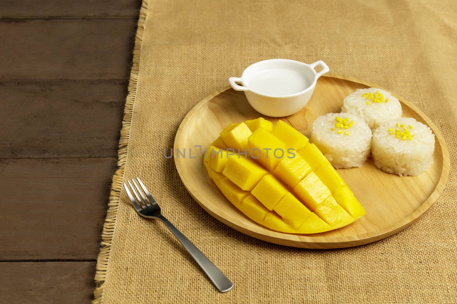 Yellow half  mango with small fork. Mango fruit cubes on the wooden table. Tropical fruit asia. Fresh yellow mango peel and Sliced cubes on wood butcher. Dessert fruit.