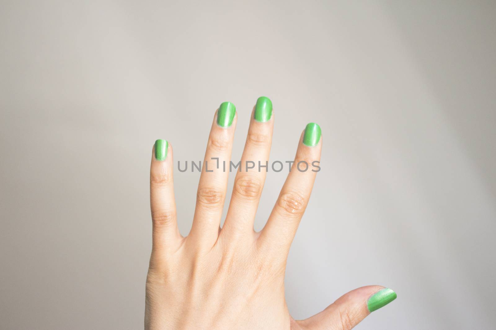 Woman hand isolated on neutral background with nails painted bright green