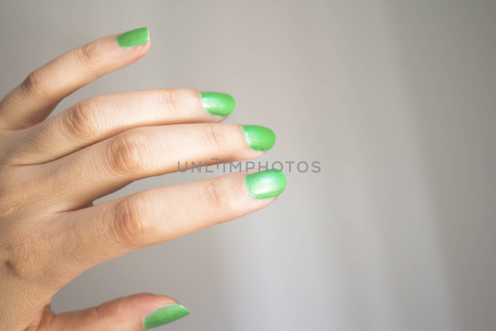 Woman hand isolated on neutral background with nails painted bright green