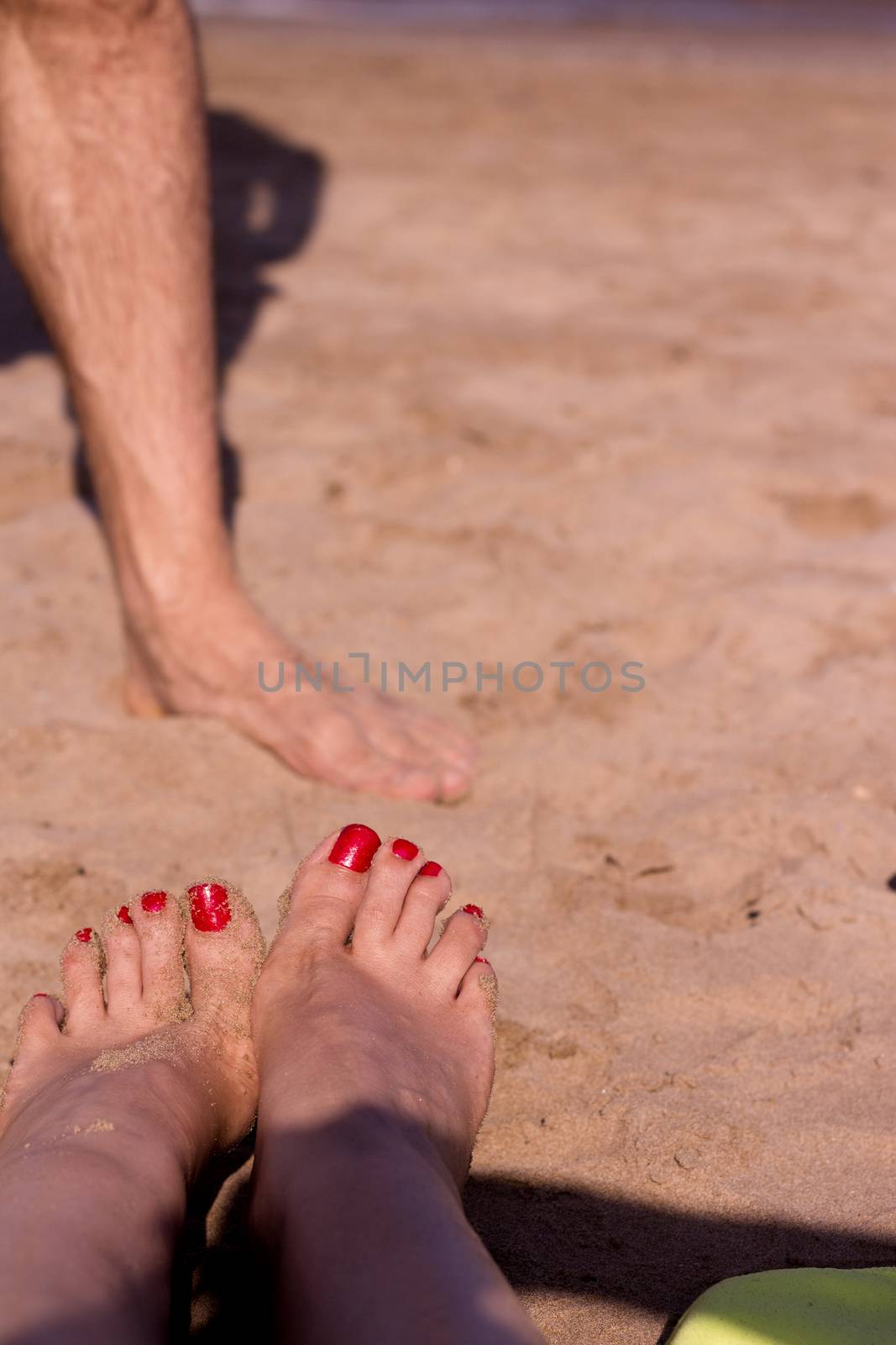 Beach scene with woman feet on the sand. Nails of feet painted red