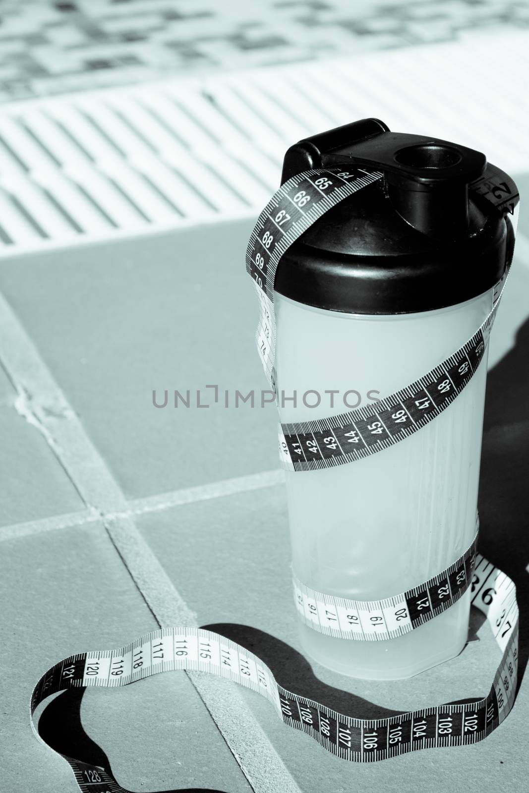 Shake mix bottle surrounded by a measuring tape on the edge of a summer pool