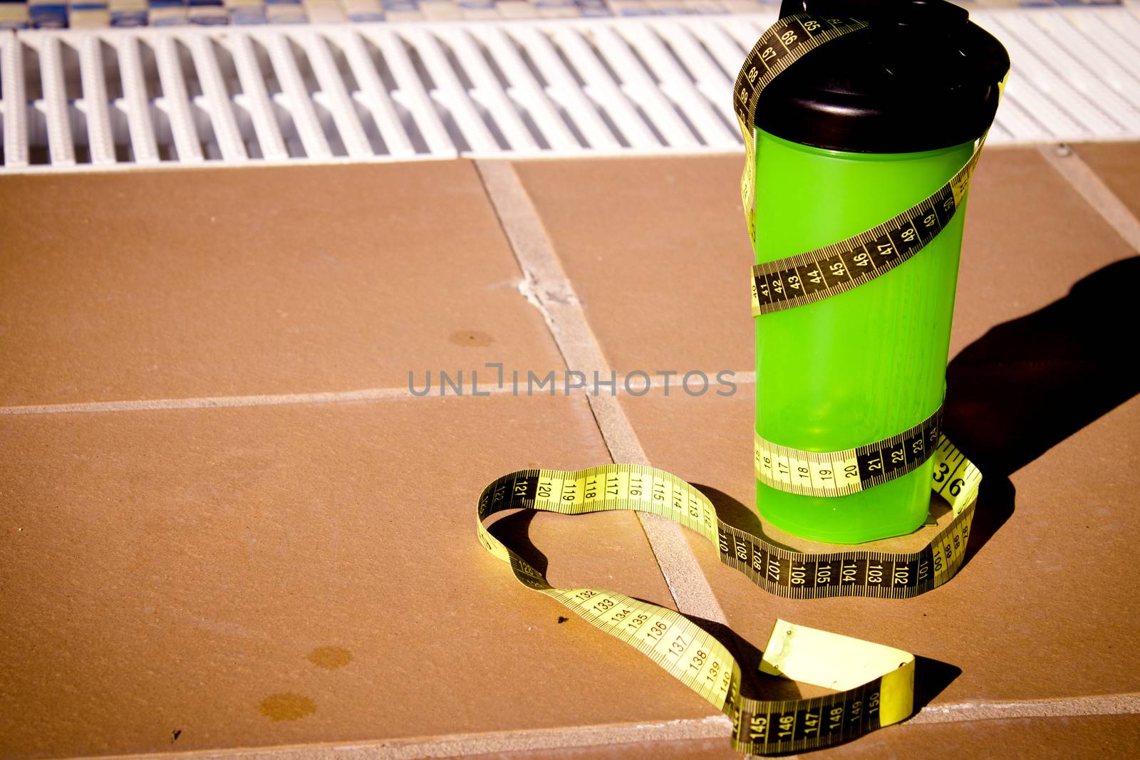 Shake mix bottle surrounded by a measuring tape on the edge of a summer pool