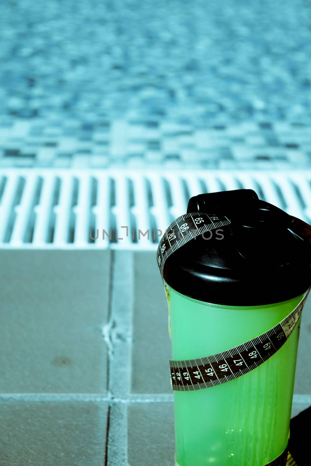 Shake mix bottle surrounded by a measuring tape on the edge of a summer pool