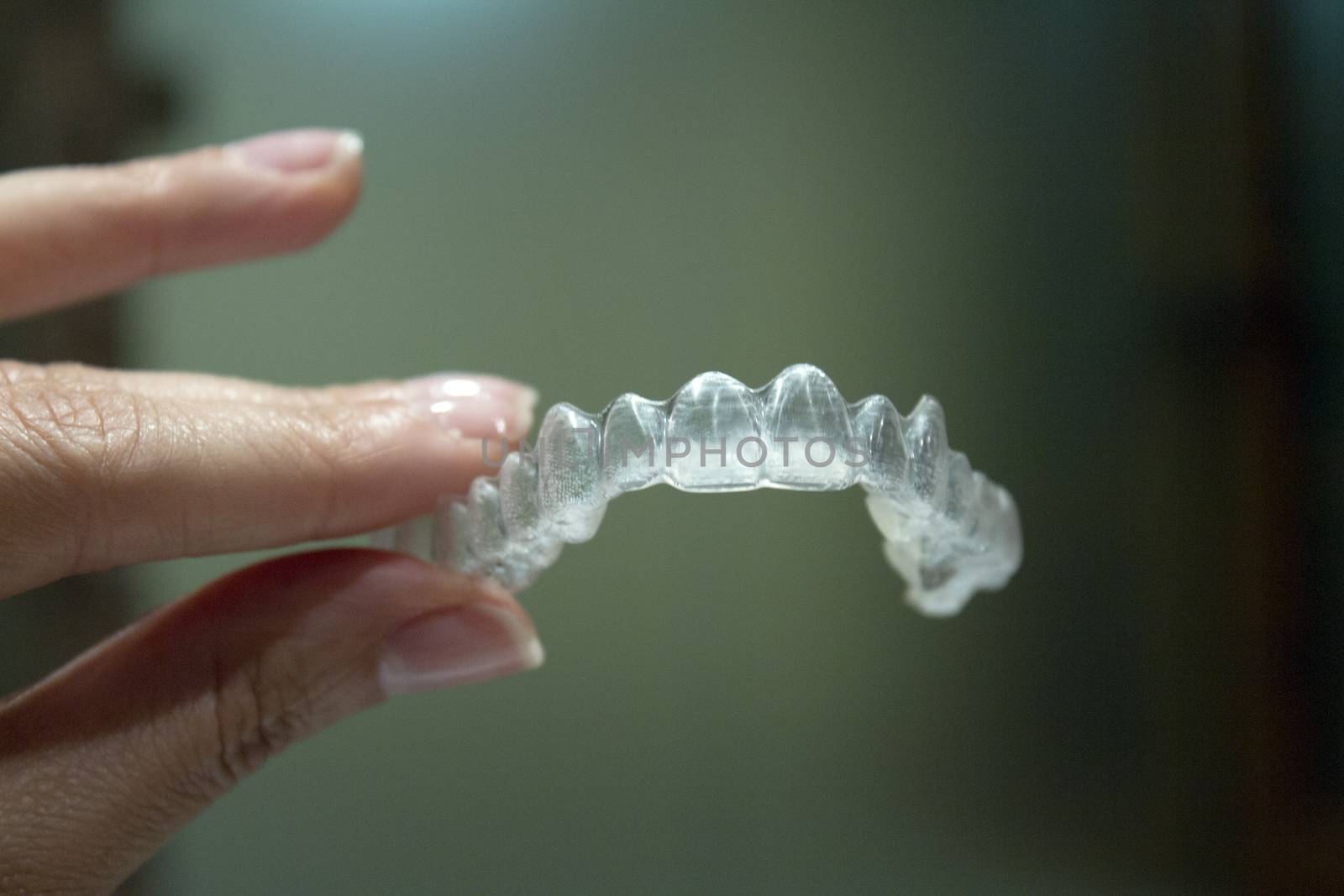 Womans hand holding transparent dental orthodontics to correct the dental alignment. Dark background