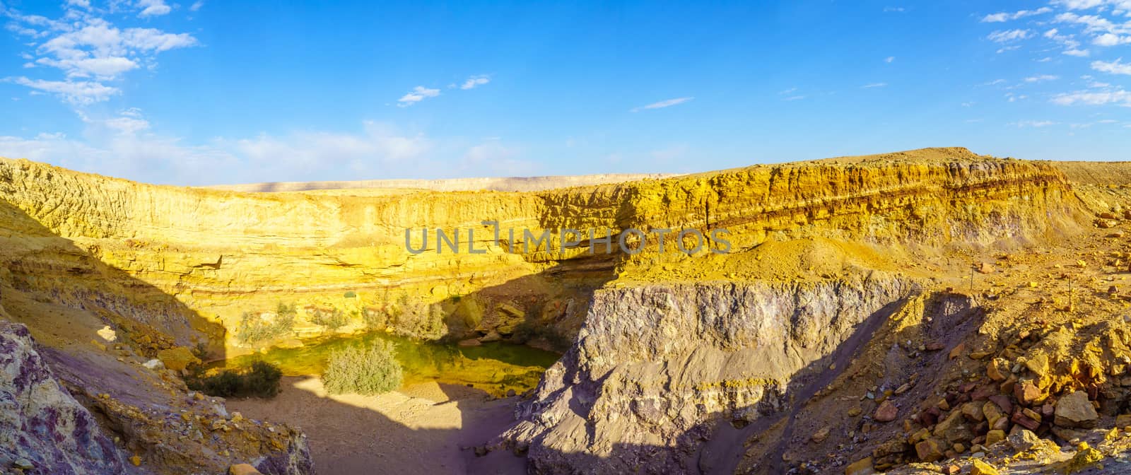Panoramic view of a water hole and layered rock formation, along the Ramon Colors Route, in Makhtesh Ramon (Ramon Crater), the Negev desert, southern Israel