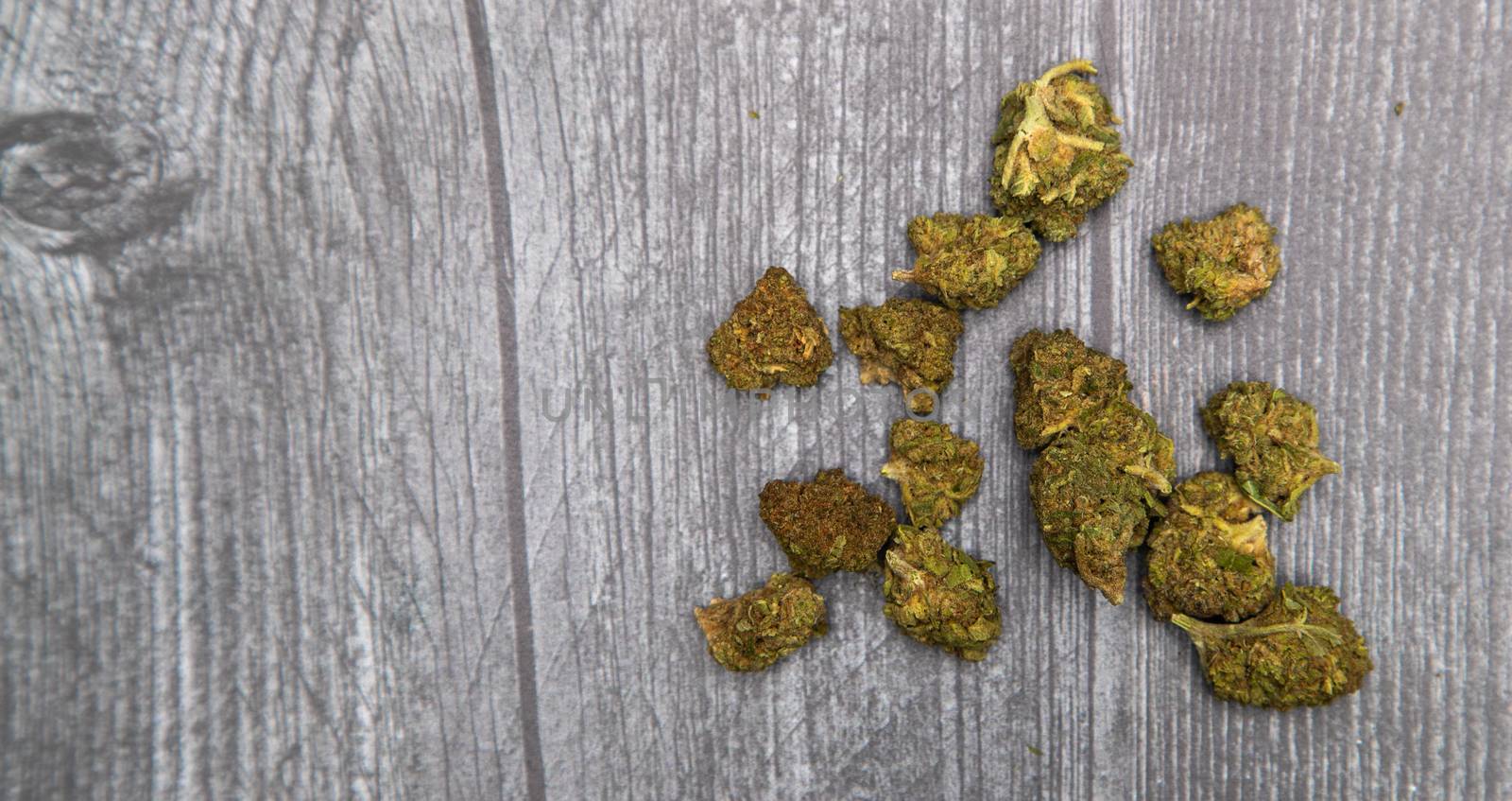 Several buds of medicinal marijuana sit on a wooden surface. Bright green with some orange and purple.