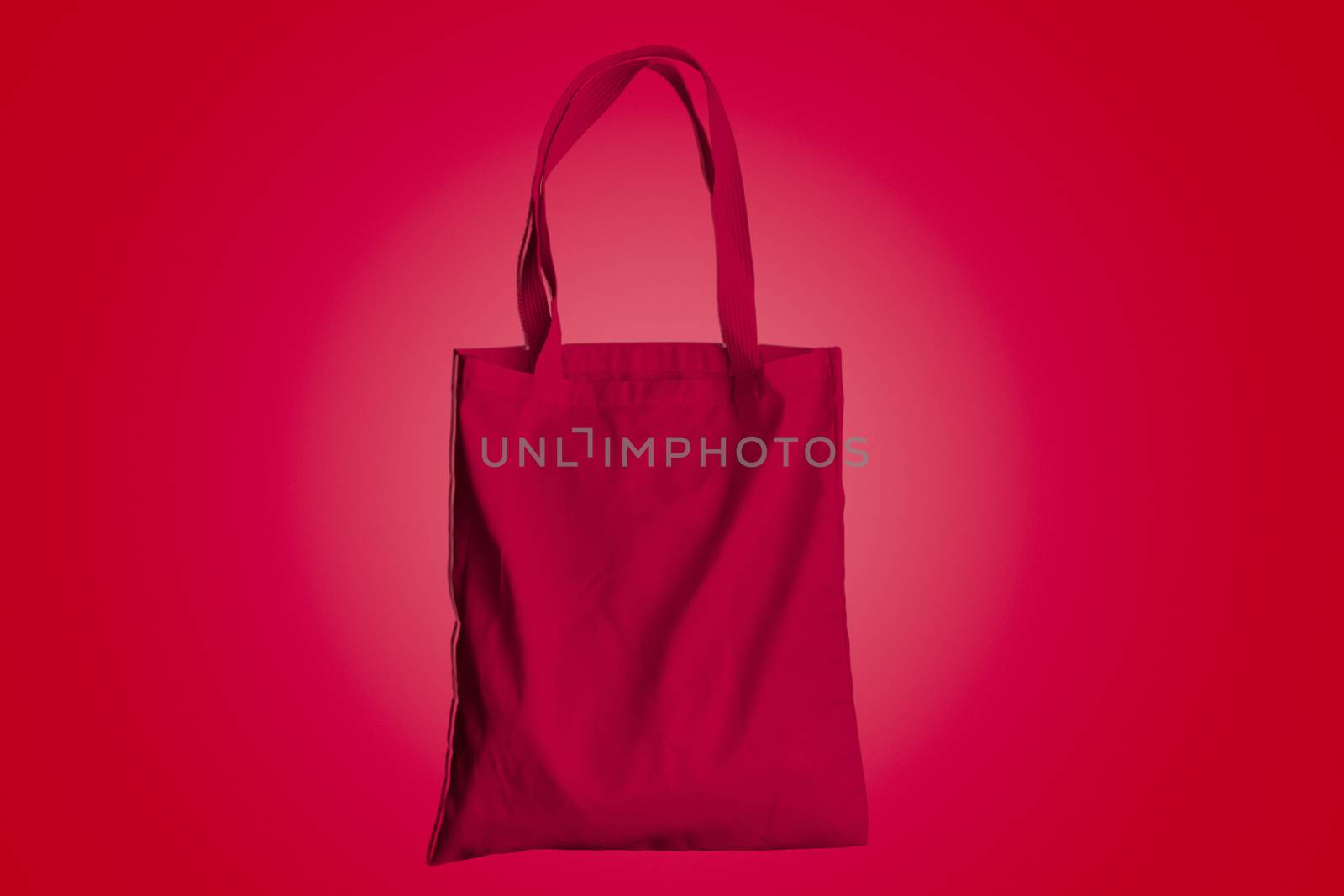 Reusable bag for groceries and shopping, red fabric tote bag on red background.