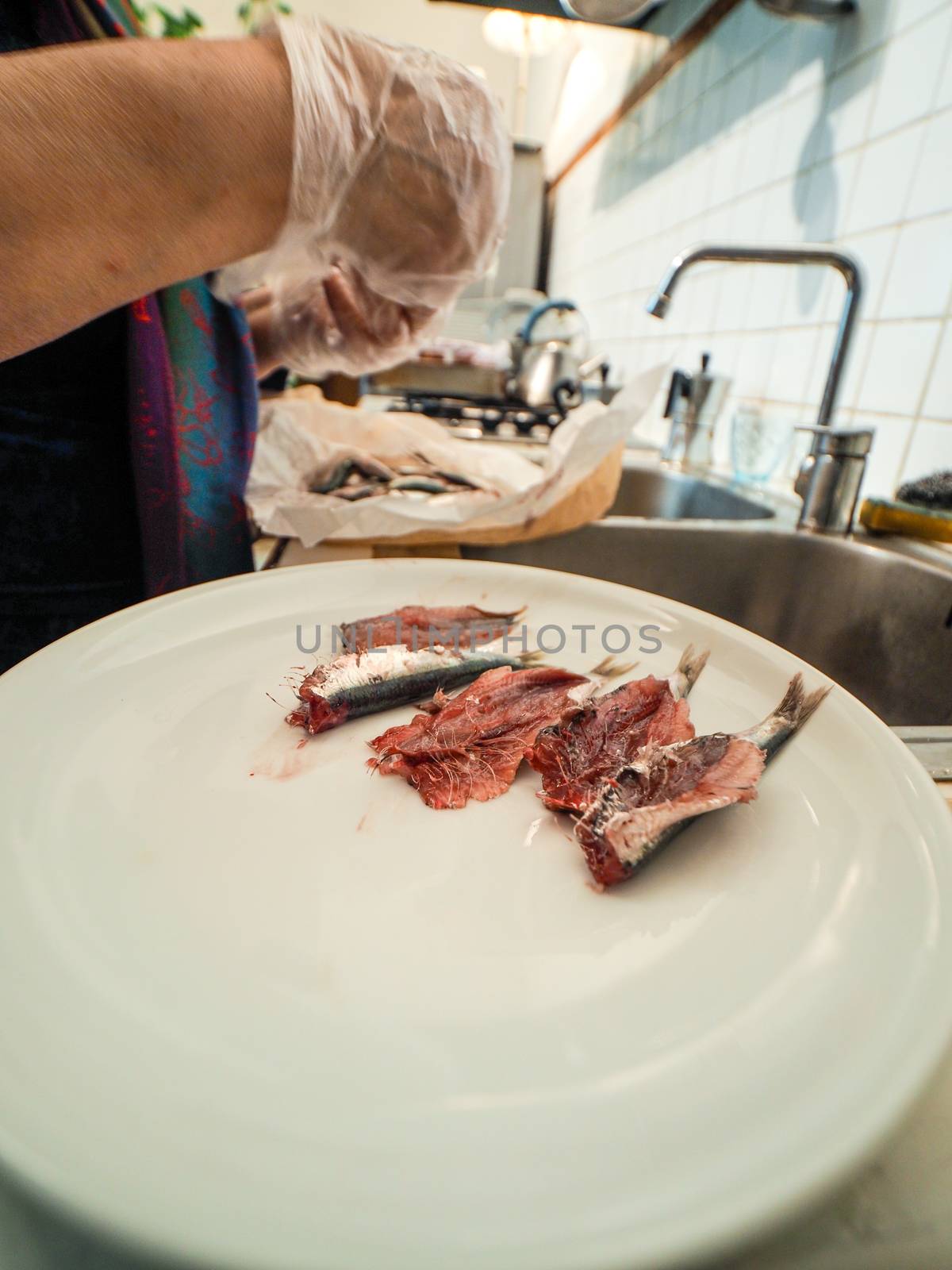 hands of senior housewive pensionate woman wearing transparent gloves cleaning anchovies fish from head and guts