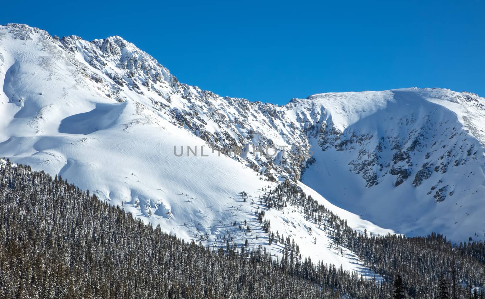 The majestic snow covered slopes of the Rocky Mountains in Colorado.  Mountains covered in snow and surrounded by forest.