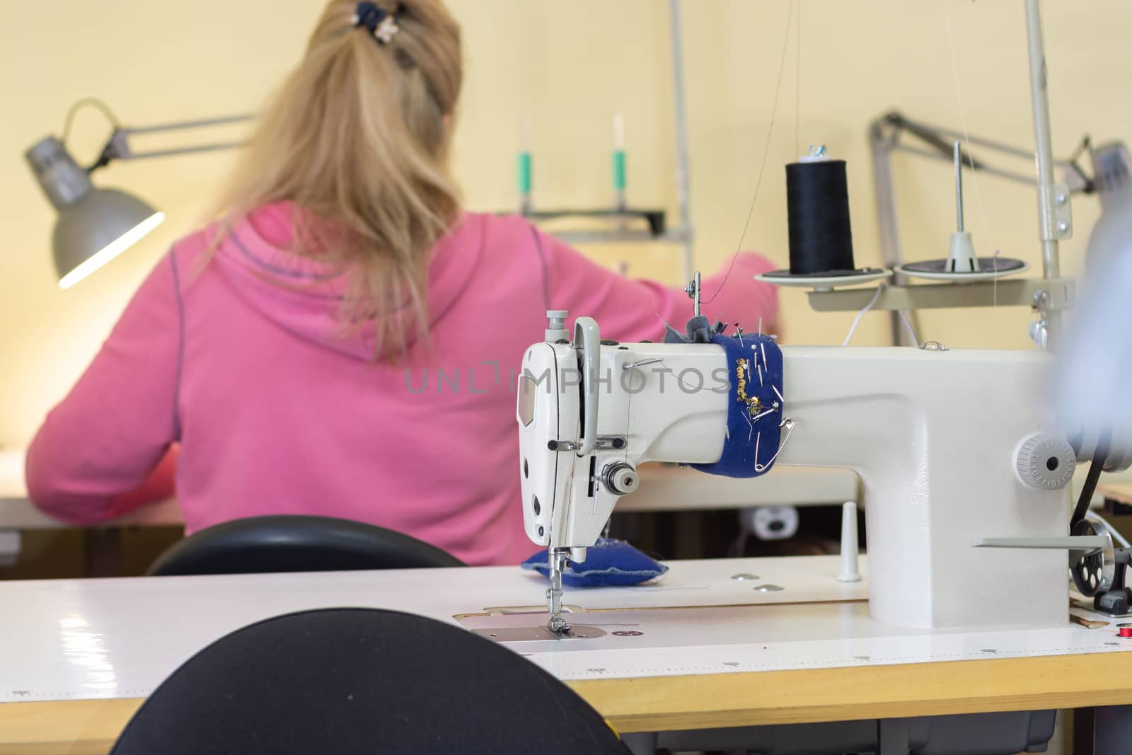 Girl sits with her back and sews on a sewing machine in a sewing shop