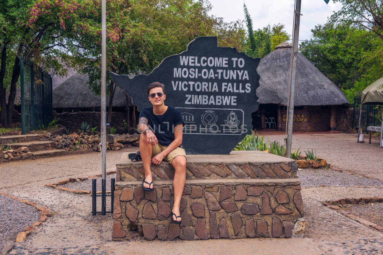 Tourist sits on the welcome sign placed at the entry of Victoria Falls, Zimbabwe by nickfox